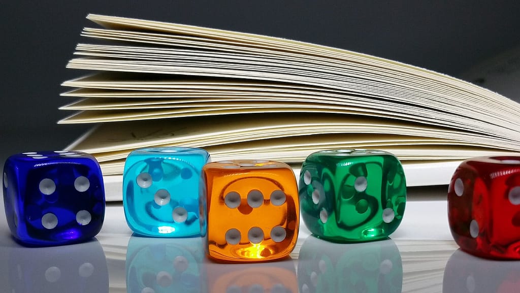 Five D6 dice on a smooth tabletop, with a book open in the background